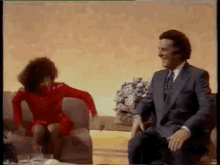 a man in a suit and tie is sitting next to a woman in a red dress .