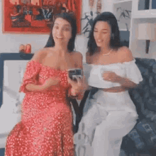 two women are sitting next to each other on a couch and smiling .
