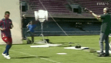 a man in a soccer uniform is running on a soccer field while a cameraman takes a picture of him
