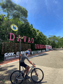 a man is riding a bike in front of a sign that says davao orienta welcome park