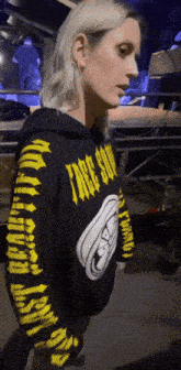 a woman wearing a black and yellow hoodie that says face down on the sleeves