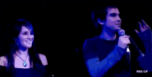 a man and a woman are standing next to each other in front of a microphone on a stage .