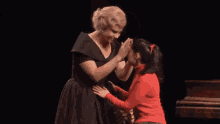 a woman in a black dress is touching the face of a woman in a red sweater