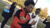 a group of young people are standing on a sidewalk . one of the young men is wearing a red and black hoodie .