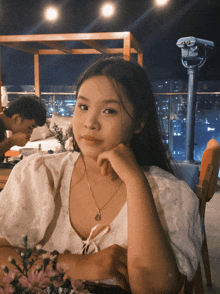 a girl sitting at a table with her hand on her face