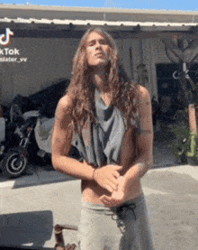 a shirtless man with long hair is standing in front of a motorcycle