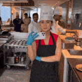 a woman wearing a chef 's hat and apron takes a selfie in a kitchen