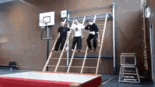 a group of people are climbing a ladder in a gym with a basketball hoop in the background