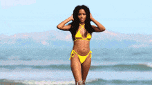 a woman in a yellow bikini is standing in front of a colorful wall .