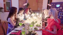 a group of women are sitting at a table with candles on it and eating food .