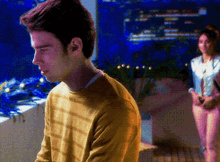 a man in a yellow sweater is standing in front of a woman in pink pants