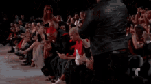 a man in a red shirt is sitting in the audience looking at his cell phone
