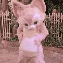 a stuffed animal in a fox costume is standing in front of a wooden fence .