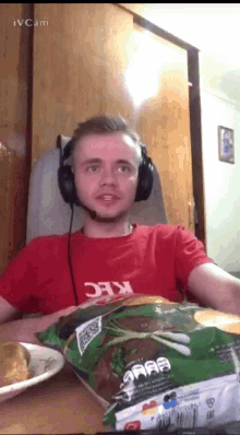 a man wearing headphones and a kfc shirt holds a bag of chips