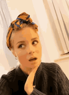 a woman wearing a black sweater and a scarf around her head has a surprised look