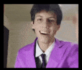 a young man wearing a purple suit and tie is smiling and making a funny face .