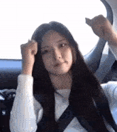 a woman with long black hair is sitting in a car with her hands in the air .