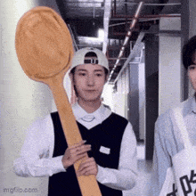a man holding a large wooden spoon in a hallway .