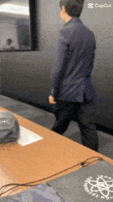 a man in a suit is walking towards a table with a capcut logo in the corner