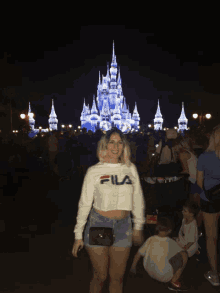 a woman wearing a fila sweatshirt stands in front of a disney castle