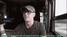 a man wearing glasses and a hat is holding a camera with the caption she 's trying
