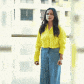 a woman wearing a yellow shirt and wide leg jeans stands in front of a window