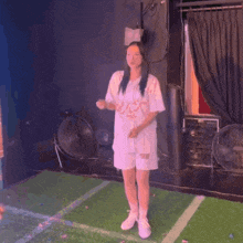 a woman in a white shirt and shorts is standing on a field with fans in the background .