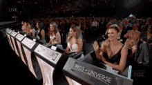 a group of women sitting in front of a miss universe podium