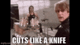 a man is standing in front of a drum set with the words `` cuts like a knife '' written below him .
