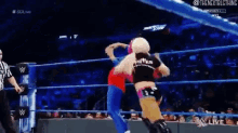 two women are wrestling in a wrestling ring with a referee in the background .