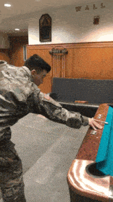 a man in a military uniform is playing pool in front of a wall with the word wall written on it