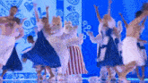 a group of people in costumes are dancing on a stage with a blue background .