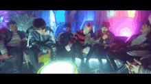 a group of young men are sitting around a table in a room with purple lights .