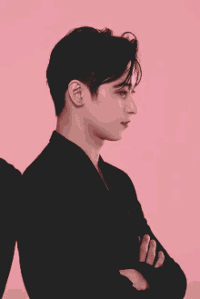 a young man in a black shirt is standing in front of a pink background