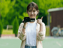 a woman is holding a sony camera and giving the thumbs up