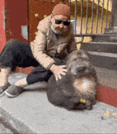 a man wearing sunglasses and a hat is petting a monkey