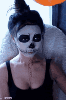a woman with a skeleton face painted on her face is sitting in front of an orange balloon