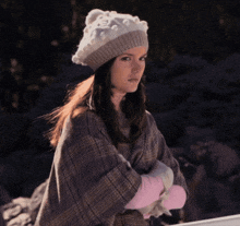 a woman wearing a plaid poncho and a hat with pom poms