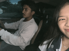 a man in a white sweater is driving a car next to a woman