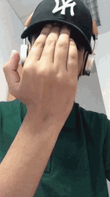 a man wearing a ny hat and headphones is covering his face with his hand