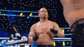 a shirtless wrestler is standing in a boxing ring with his hands on his chest .