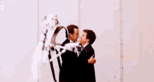 two men in suits are hugging each other in front of a wall .
