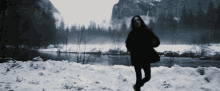 a woman standing in the snow near a river