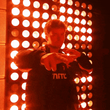 a man wearing a black shirt that says ' nftc ' on it stands in front of a wall of red lights