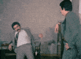 two men in suits are dancing in a room with a patterned wallpaper