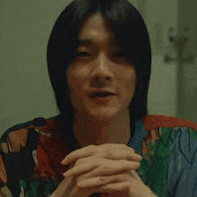 a young man with his hands folded looks at the camera