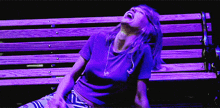 a woman in a purple shirt is laughing while sitting on a wooden bench