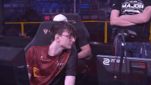 a man wearing a major shirt sits in a gaming chair
