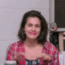 a woman in a plaid shirt is sitting at a table with her hands in the air .