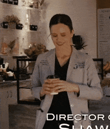 a woman holding a cup of coffee in front of a sign that says director